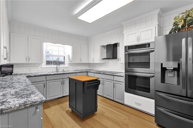 kitchen with wall chimney range hood, sink, light wood-type flooring, a kitchen island, and stainless steel appliances