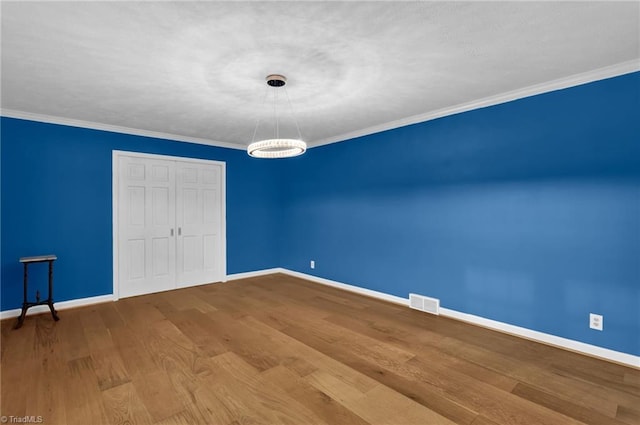 spare room with a chandelier, hardwood / wood-style flooring, and ornamental molding