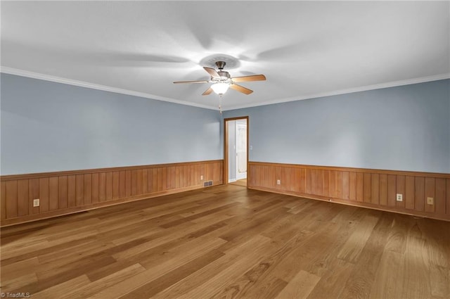 spare room with ceiling fan, light hardwood / wood-style flooring, wood walls, and ornamental molding