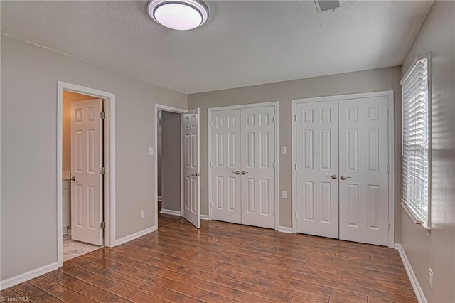 unfurnished bedroom featuring wood-type flooring, a textured ceiling, two closets, and multiple windows