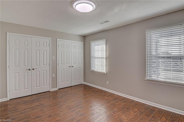 unfurnished bedroom featuring a textured ceiling, multiple closets, and dark wood-type flooring