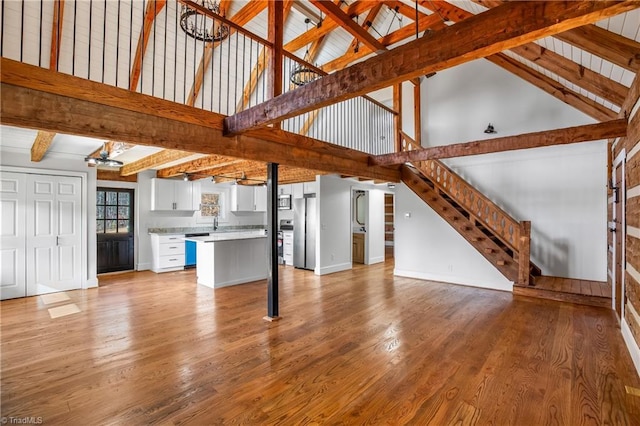 unfurnished living room featuring beamed ceiling, light wood-style flooring, baseboards, and stairs