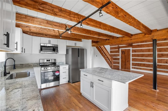 kitchen featuring stainless steel appliances, a sink, light wood-style floors, beam ceiling, and light stone countertops