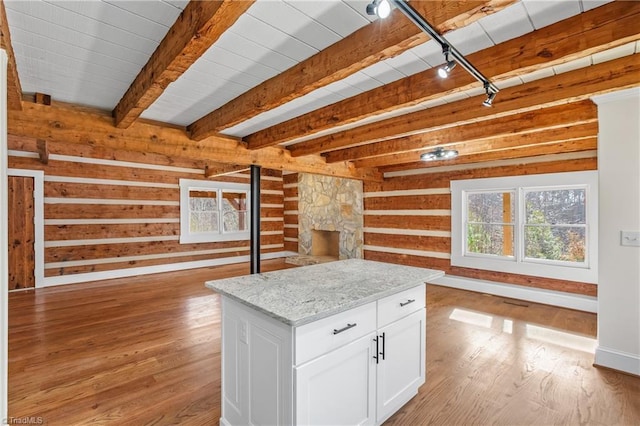 interior space with light wood-style flooring, white cabinetry, open floor plan, and beamed ceiling