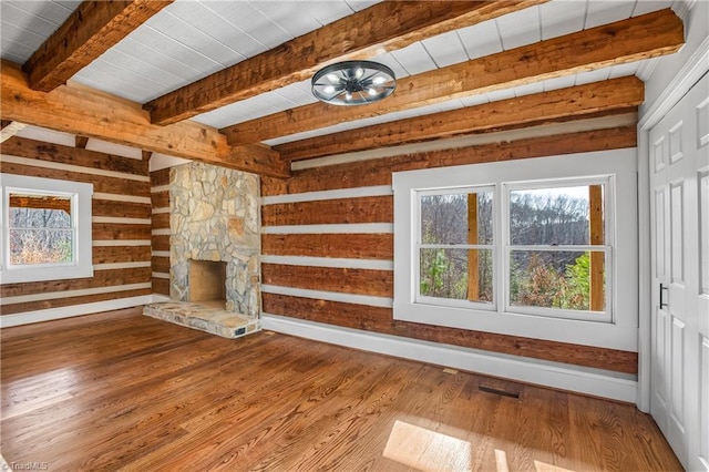 unfurnished living room with a wealth of natural light, a fireplace, beamed ceiling, and wood finished floors