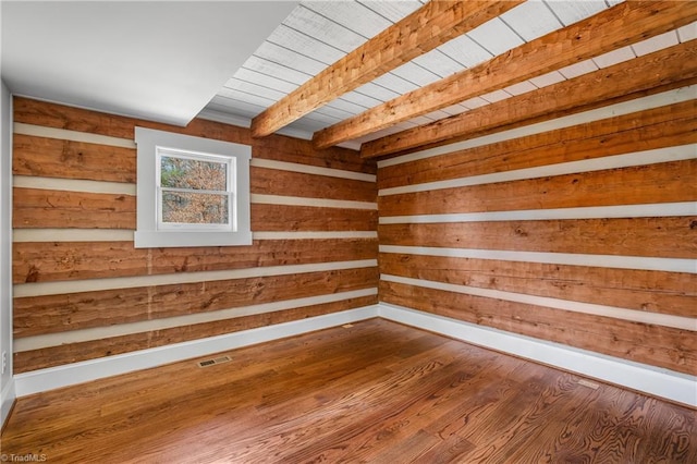 empty room featuring wooden ceiling, wood walls, wood finished floors, visible vents, and beam ceiling