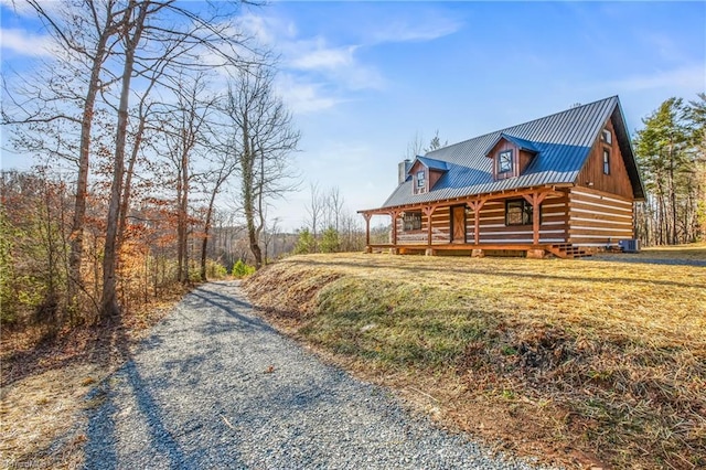 view of side of home featuring gravel driveway, covered porch, central AC unit, metal roof, and log exterior