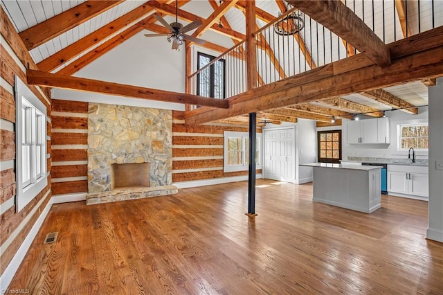 unfurnished living room featuring ceiling fan, light wood-style flooring, a fireplace, visible vents, and beamed ceiling