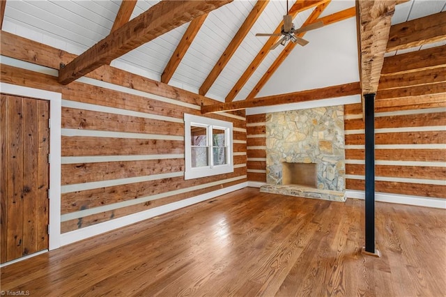 unfurnished living room featuring wooden walls, ceiling fan, wood finished floors, a fireplace, and beam ceiling