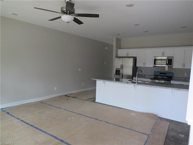 kitchen with dark stone counters, appliances with stainless steel finishes, sink, white cabinets, and ceiling fan