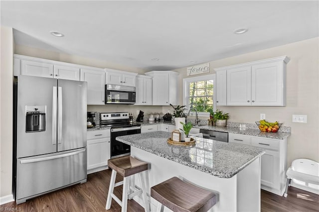 kitchen with white cabinets, dark hardwood / wood-style flooring, appliances with stainless steel finishes, a kitchen island, and light stone countertops