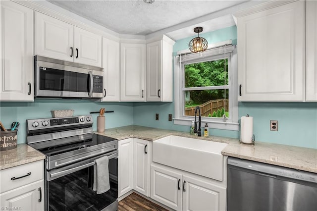 kitchen with light stone counters, stainless steel appliances, white cabinetry, a sink, and a textured ceiling