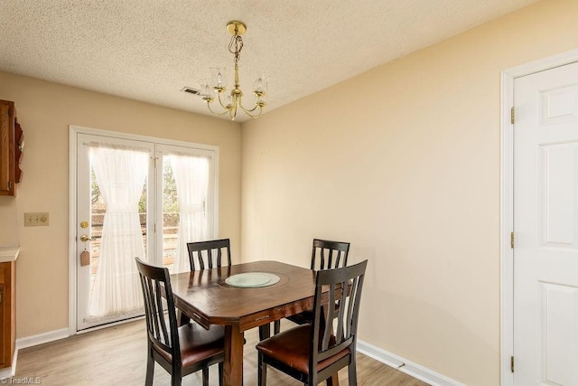 dining area with an inviting chandelier, a textured ceiling, and light hardwood / wood-style flooring