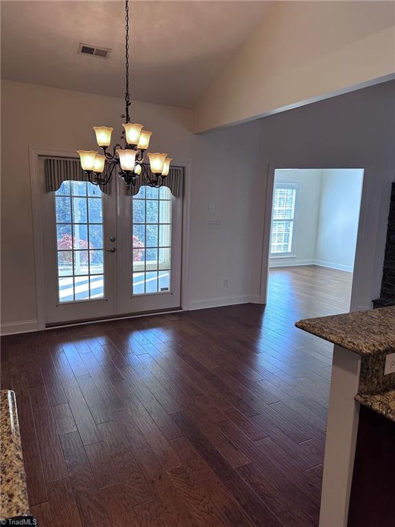 unfurnished dining area featuring lofted ceiling, dark hardwood / wood-style floors, and an inviting chandelier