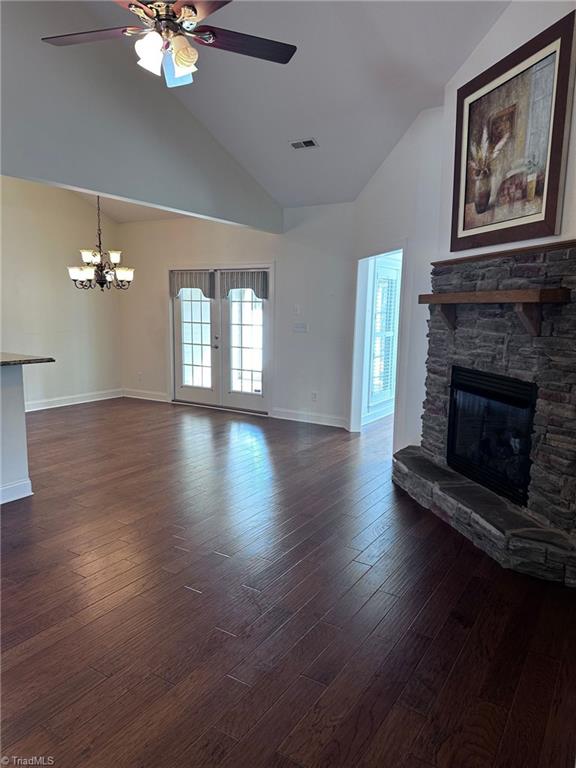 unfurnished living room with a stone fireplace, dark wood-type flooring, ceiling fan with notable chandelier, and high vaulted ceiling