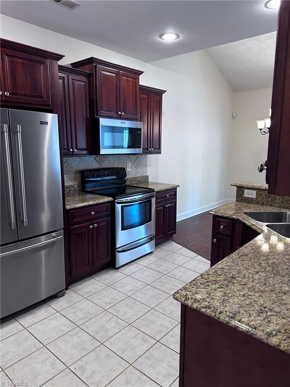 kitchen featuring tasteful backsplash, appliances with stainless steel finishes, stone countertops, and sink