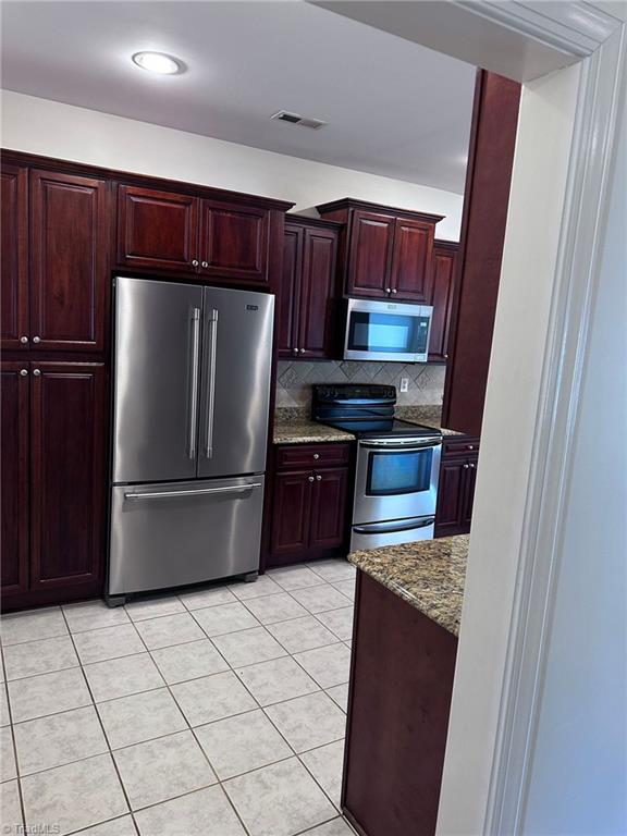 kitchen featuring light tile patterned floors, decorative backsplash, light stone countertops, and appliances with stainless steel finishes