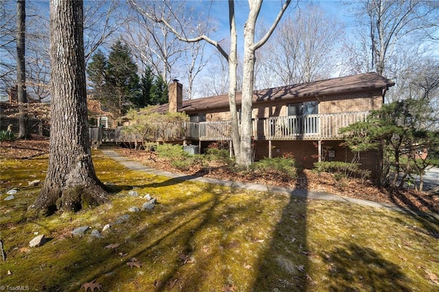 rear view of house featuring a yard, brick siding, a chimney, and a wooden deck