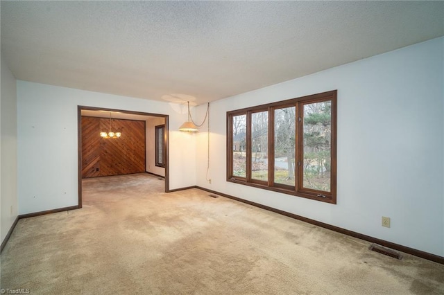 spare room with baseboards, visible vents, light colored carpet, a textured ceiling, and wood walls