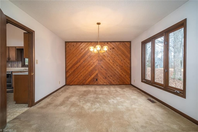 unfurnished dining area featuring visible vents, light colored carpet, an accent wall, wooden walls, and a chandelier