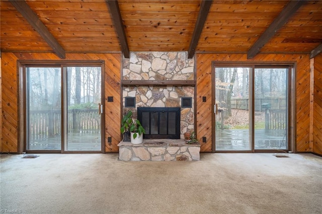 unfurnished living room featuring carpet floors, wooden walls, and a stone fireplace