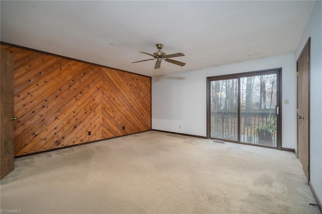 spare room featuring baseboards, ceiling fan, wood walls, and light colored carpet