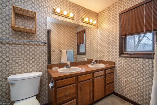 bathroom featuring double vanity, a sink, toilet, and wallpapered walls