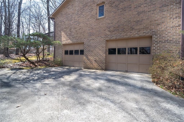 view of property exterior featuring a garage, brick siding, and aphalt driveway