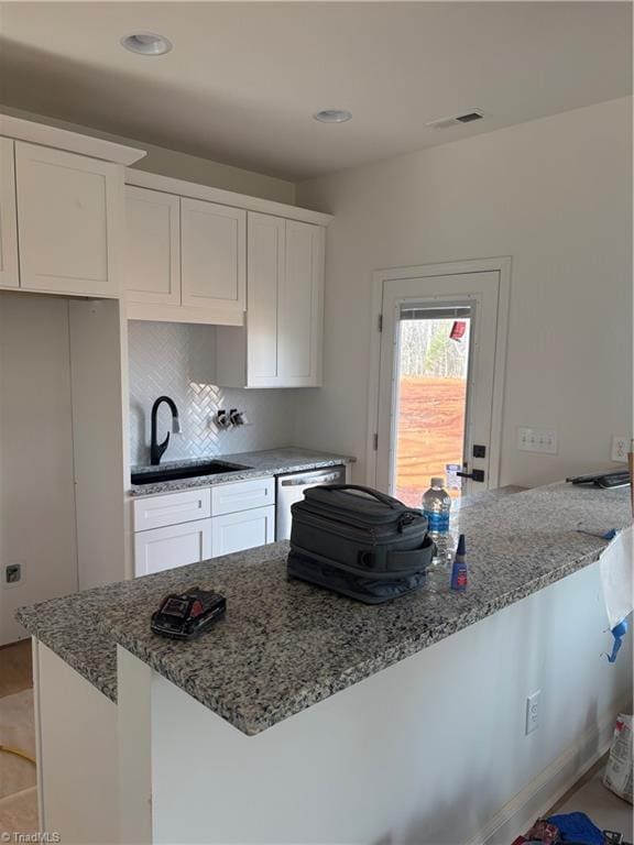 kitchen with light stone counters, visible vents, stainless steel dishwasher, white cabinetry, and a sink