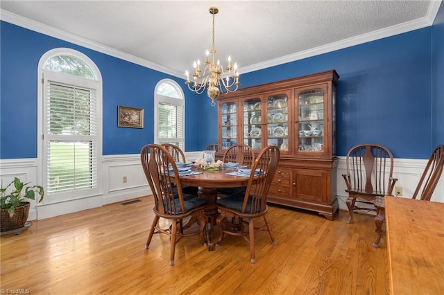 6516 Dornoch Dr, Greensboro, NC 27410 - dining room featuring a chandelier, light wood-type flooring, a wainscoted wall, ornamental molding, and a decorative wall