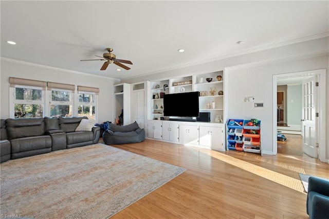 living room featuring built in shelves, ceiling fan, ornamental molding, and light hardwood / wood-style floors