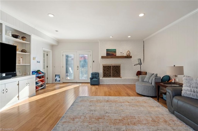 living room featuring crown molding, french doors, a brick fireplace, and light wood-type flooring