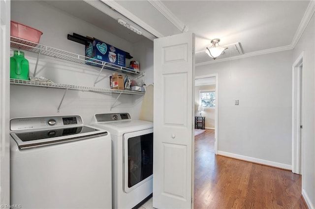 clothes washing area with ornamental molding, washer and clothes dryer, and hardwood / wood-style floors