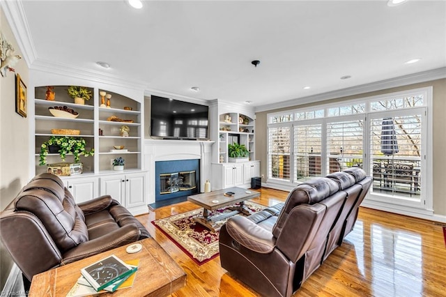 living area with recessed lighting, light wood-type flooring, a glass covered fireplace, and crown molding