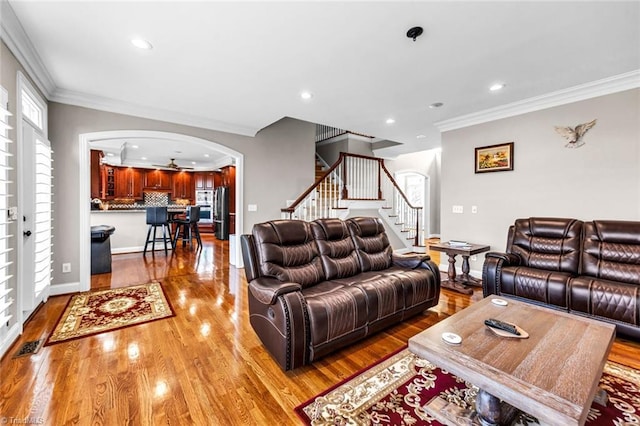 living area with arched walkways, recessed lighting, ornamental molding, light wood-type flooring, and stairs