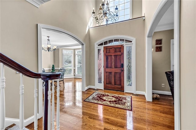 entryway with arched walkways, baseboards, wood finished floors, and an inviting chandelier