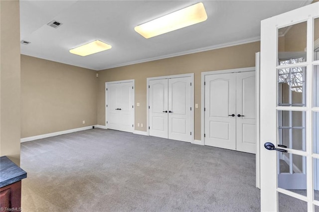 unfurnished bedroom with carpet floors, visible vents, baseboards, and two closets