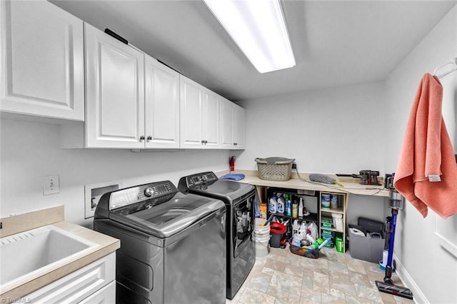 clothes washing area with cabinet space, baseboards, washing machine and clothes dryer, stone finish flooring, and a sink