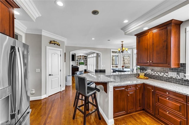 kitchen with arched walkways, dark wood-style flooring, freestanding refrigerator, a peninsula, and light stone countertops