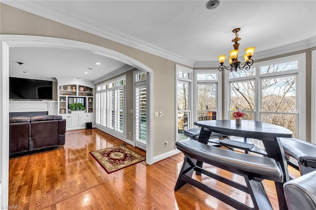 dining room with built in shelves, an inviting chandelier, ornamental molding, wood finished floors, and baseboards