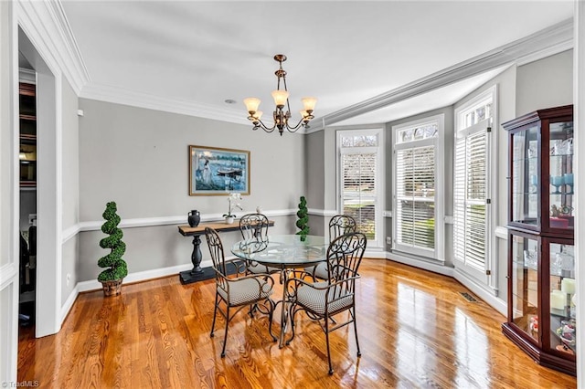 dining space featuring baseboards, visible vents, wood finished floors, crown molding, and a chandelier