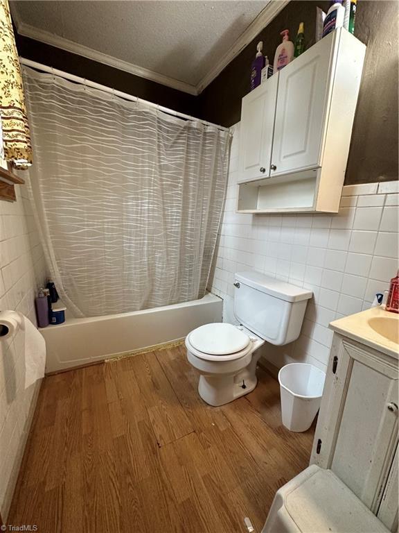 full bathroom with wood-type flooring, ornamental molding, and shower / bath combo with shower curtain