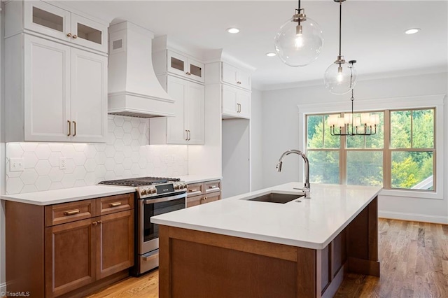 kitchen featuring sink, white cabinets, custom exhaust hood, gas stove, and a center island with sink