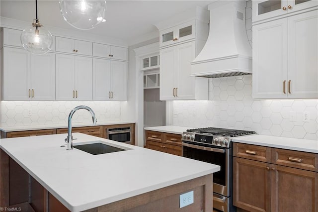 kitchen with premium range hood, appliances with stainless steel finishes, sink, backsplash, and a center island with sink