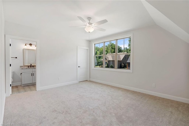 unfurnished bedroom with ceiling fan, vaulted ceiling, light colored carpet, and ensuite bath