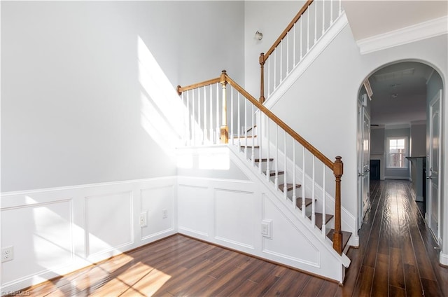 stairs featuring arched walkways, a decorative wall, crown molding, and wood finished floors