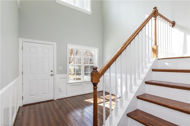 entrance foyer featuring dark wood-type flooring, wainscoting, a healthy amount of sunlight, and a decorative wall