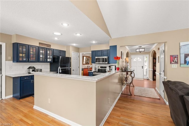 kitchen featuring blue cabinets, appliances with stainless steel finishes, a peninsula, light wood finished floors, and glass insert cabinets