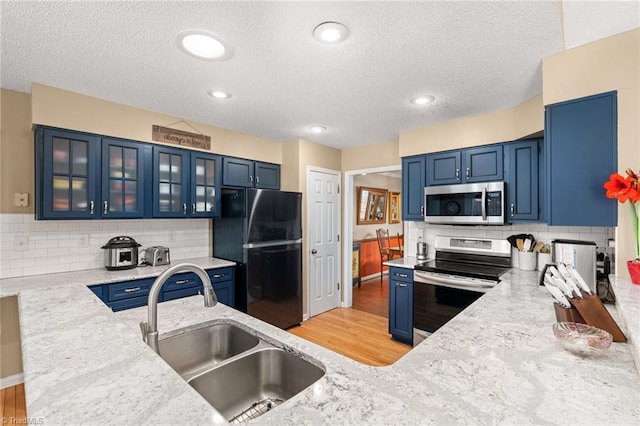 kitchen featuring light stone countertops, a sink, stainless steel appliances, blue cabinets, and light wood-type flooring