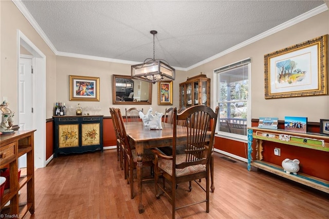 dining space with a textured ceiling, wood finished floors, visible vents, and ornamental molding